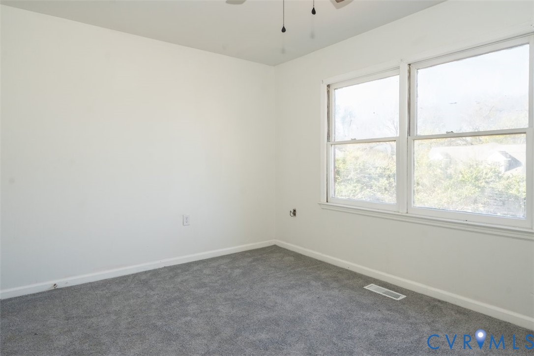 Neutral-toned carpeting, white walls, and large windows providing natural light, finished with an attached ceiling fan