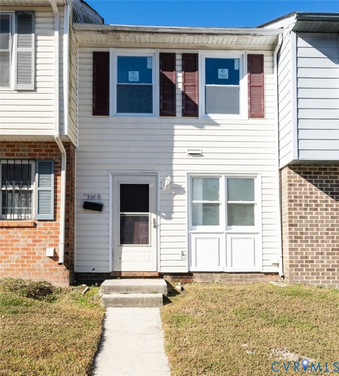 Exterior facade featuring horizontal siding, decorative shutters, brick masonry accents, and a concrete walkway