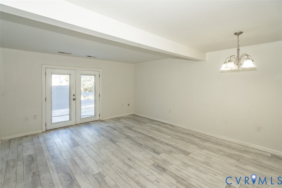 Interior space featuring wood-finish flooring, double glass panel doors, and a multi-arm metal chandelier with frosted glass shades Interior space featuring wood-finish flooring, double glass panel doors, and a multi-arm metal chandelier with frosted glass shades