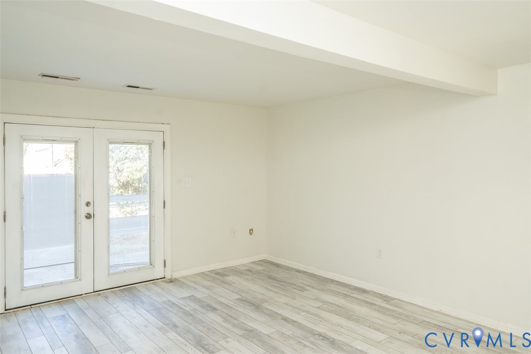 Neutral interior space featuring wood-finish flooring, white walls, and white French doors with glass inserts Neutral interior space featuring wood-finish flooring, white walls, and white French doors with glass inserts