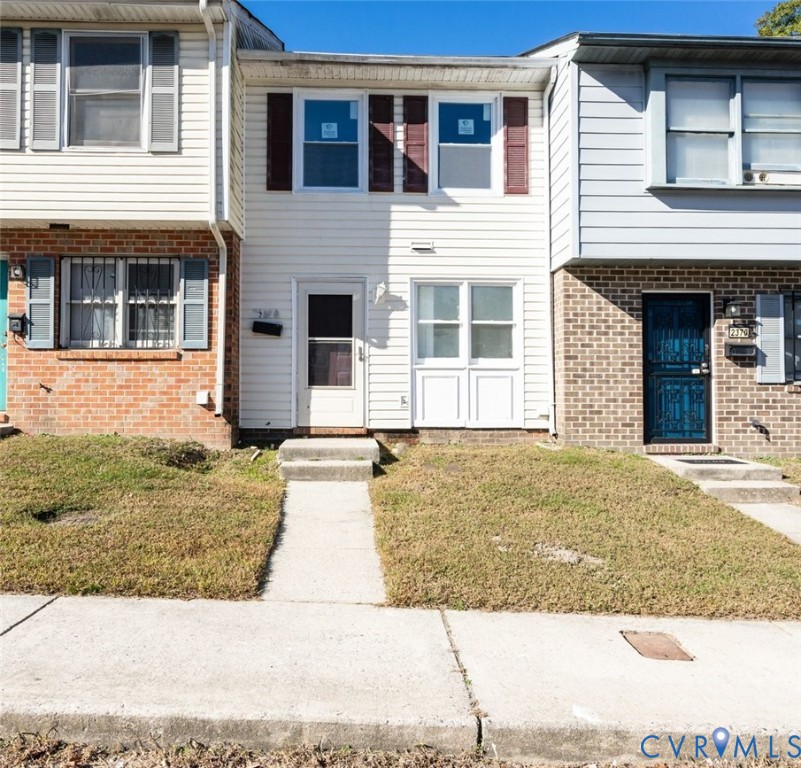 Multi-level townhome exterior featuring horizontal vinyl siding, dual-pane windows with decorative shutters, and concrete front entry steps Multi-level townhome exterior featuring horizontal vinyl siding, dual-pane windows with decorative shutters, and concrete front entry steps