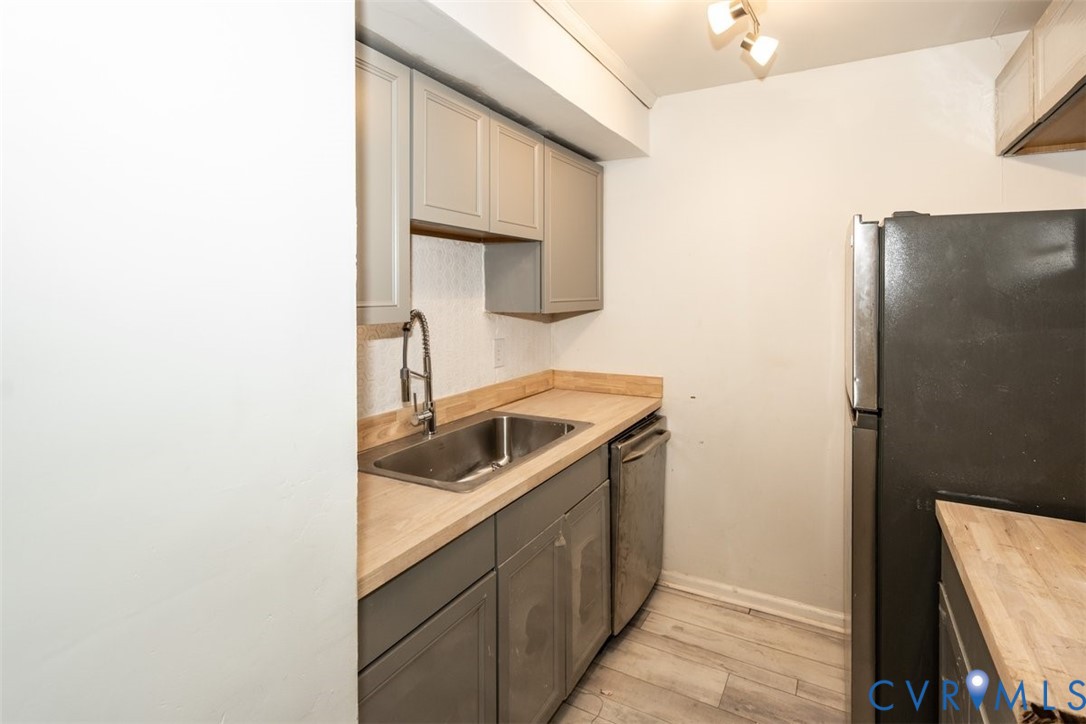 Kitchen featuring grey cabinetry, wood-finish countertops, stainless steel sink with a high-arc faucet, integrated dishwasher, and wood-finish flooring Kitchen featuring grey cabinetry, wood-finish countertops, stainless steel sink with a high-arc faucet, integrated dishwasher, and wood-finish flooring