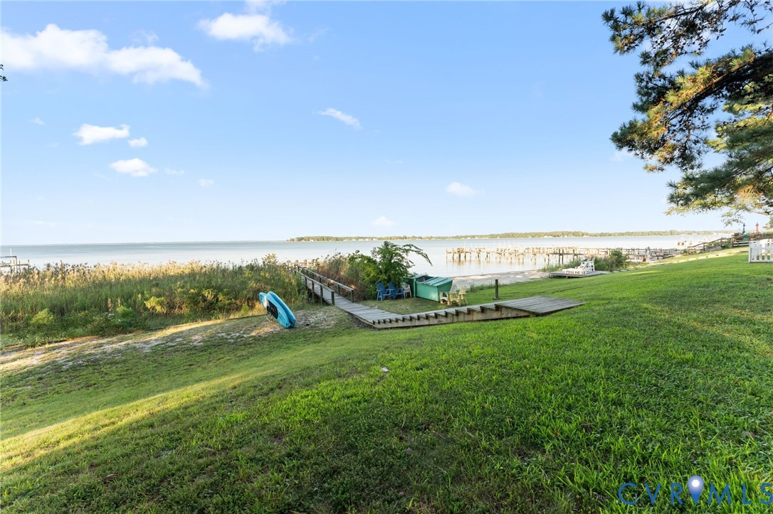 Waterfront lot featuring a sloping grass lawn, mature trees, and a wooden pier