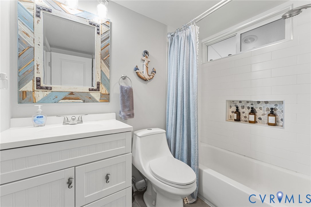 Bathroom featuring a white vanity with beadboard detailing, a rectangular basin, a tub-shower combination with white subway tile surround, and a recessed stone-tiled shower niche