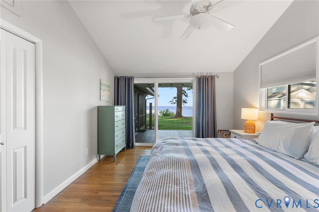 Vaulted ceiling with integrated paddle fan, wood-finish flooring, sliding glass door, and natural water backdrop