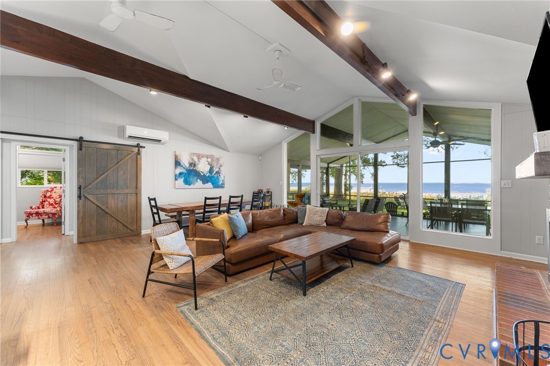 Vaulted ceilings featuring exposed wood-finish beams, wall-to-wall floor-to-ceiling windows, wood-finish flooring, sliding barn door, and wall-mounted climate control unit