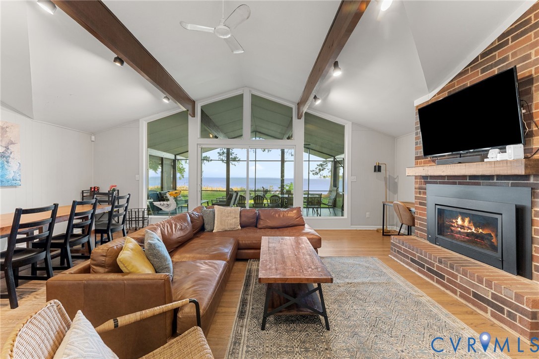 Vaulted ceilings with exposed wooden beams, brick fireplace with a custom wood mantel, wood-finish flooring, and expansive floor-to-ceiling windows Vaulted ceilings with exposed wooden beams, brick fireplace with a custom wood mantel, wood-finish flooring, and expansive floor-to-ceiling windows