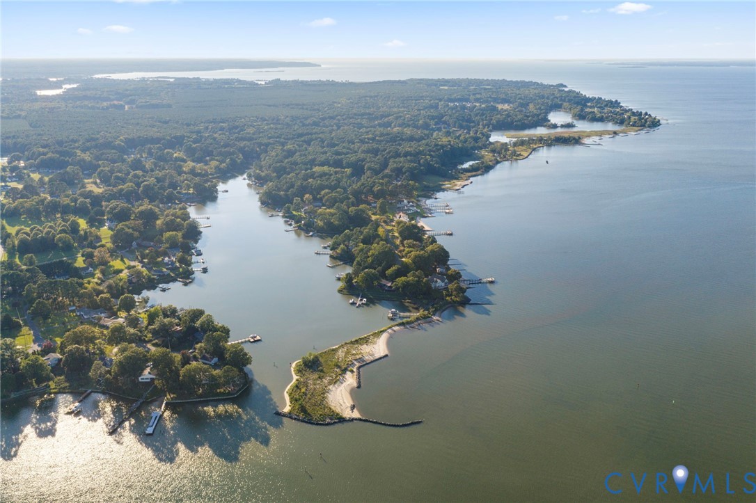 Aerial perspective of waterfront peninsula featuring natural sand shoreline, mature wooded landscape, and multiple private wooden piers extending into the bay