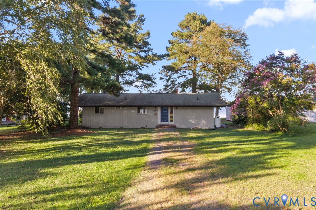 Single-story residence featuring light-toned horizontal siding, a covered entryway, and a low-pitched roof, set upon a spacious lot with mature trees