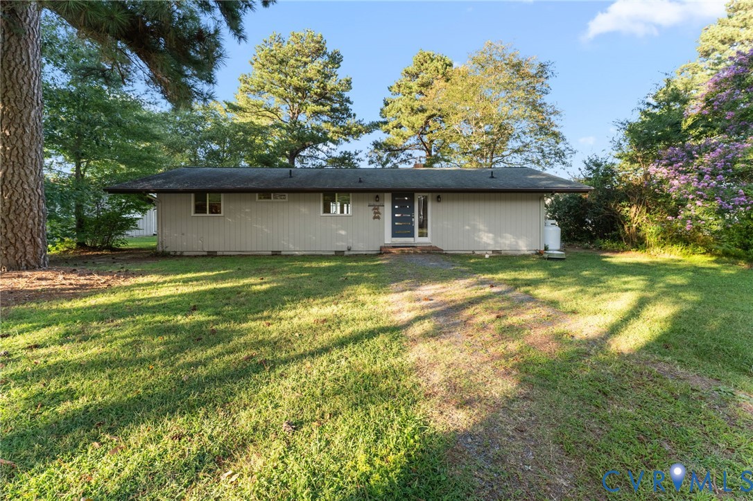 Single-story exterior featuring a low-pitch roofline, vertical siding, an entrance with glass sidelights, and a spacious front lawn with mature trees