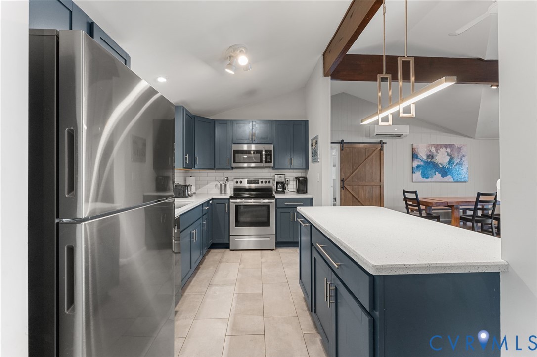 Kitchen featuring blue cabinetry, stainless steel appliances, stone-surface island, ceramic tile flooring, and exposed ceiling beams