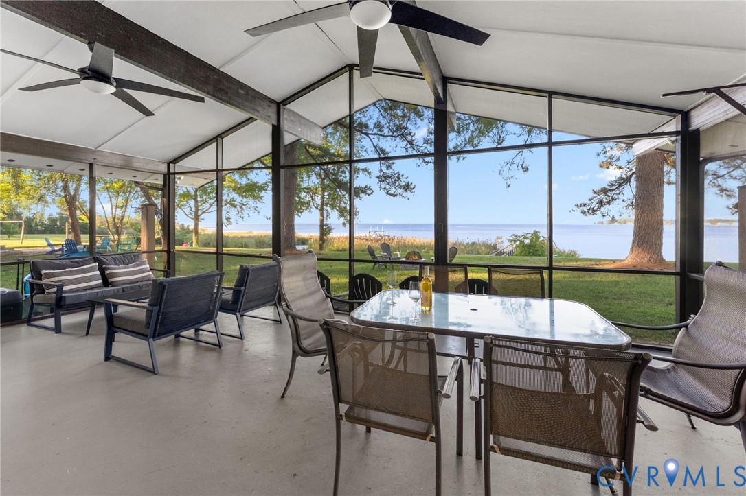 Screened-in porch featuring vaulted ceilings with exposed dark-finish beams, ceiling fans, and expansive floor-to-ceiling screen panels overlooking the waterfront