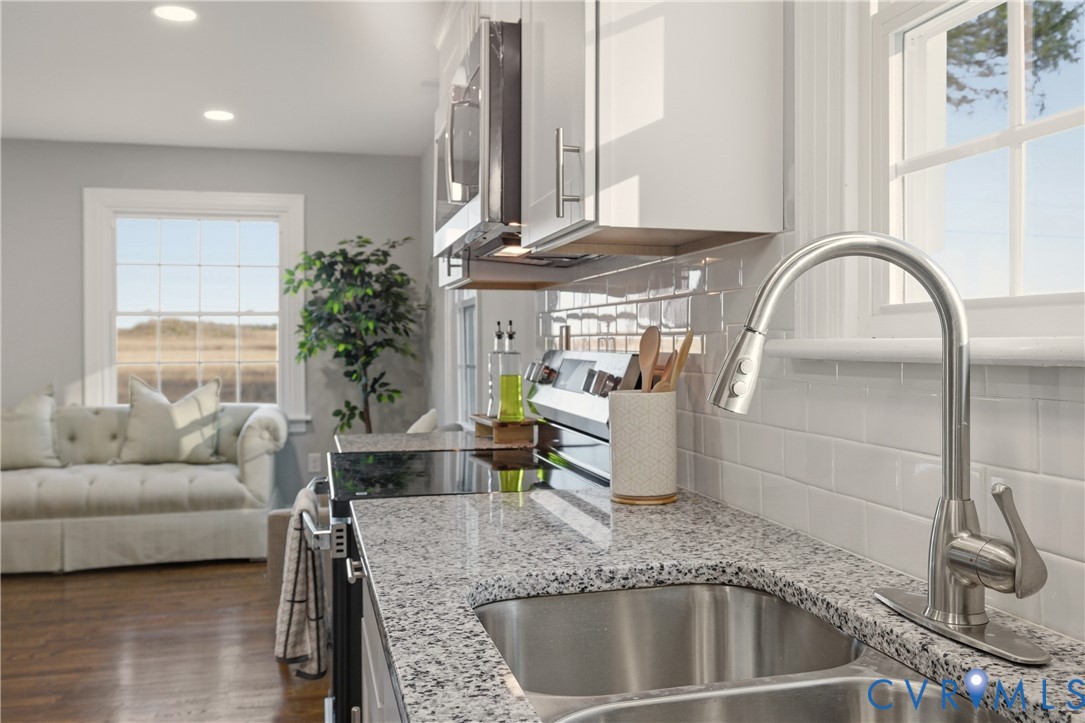 Kitchen featuring stone countertops, stainless steel undermount double sink, brushed nickel high-arc pull-down faucet, white subway tile backsplash, and white cabinetry