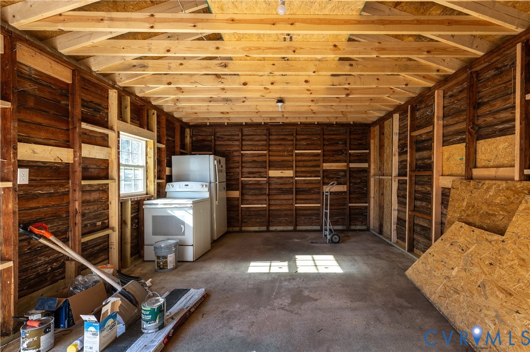Interior space featuring exposed wood-frame wall construction, vaulted rafters, concrete flooring, and a single-pane window