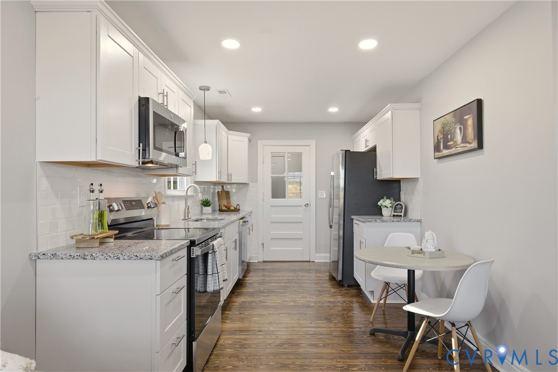 Kitchen featuring white shaker-style cabinetry, speckled stone-finish countertops, stainless steel appliances, white subway tile backsplash, and wood-finish flooring