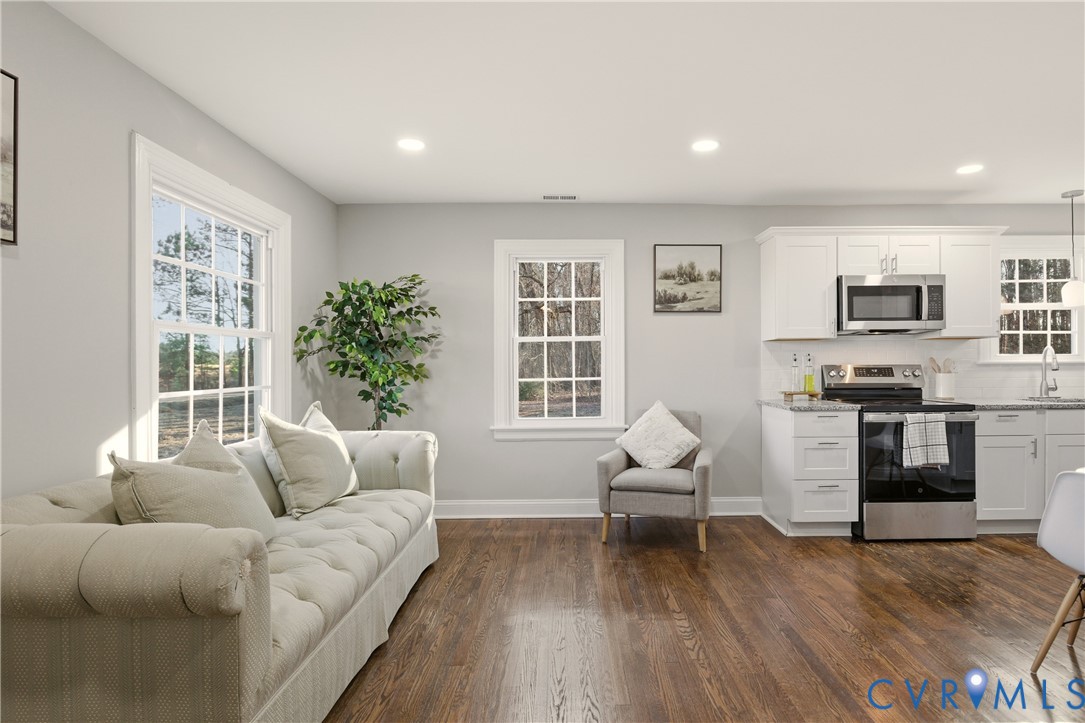 Open-concept interior featuring wood-finish flooring, white shaker-style cabinetry, stainless steel appliances, and multi-pane windows
