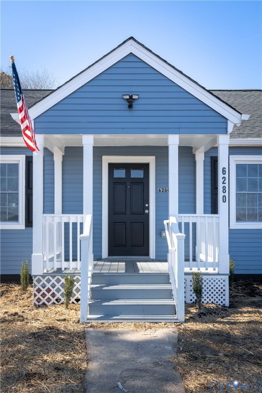Front exterior featuring blue horizontal siding, white trim, a covered porch with white railing, lattice skirting, and a dark multi-panel entry door