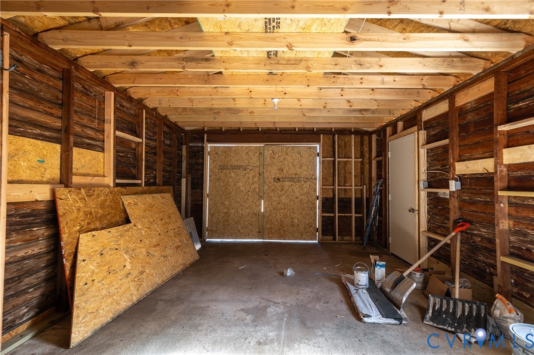Detached structure with an exposed timber-frame ceiling, wood-plank walls, concrete flooring, and double-door entry