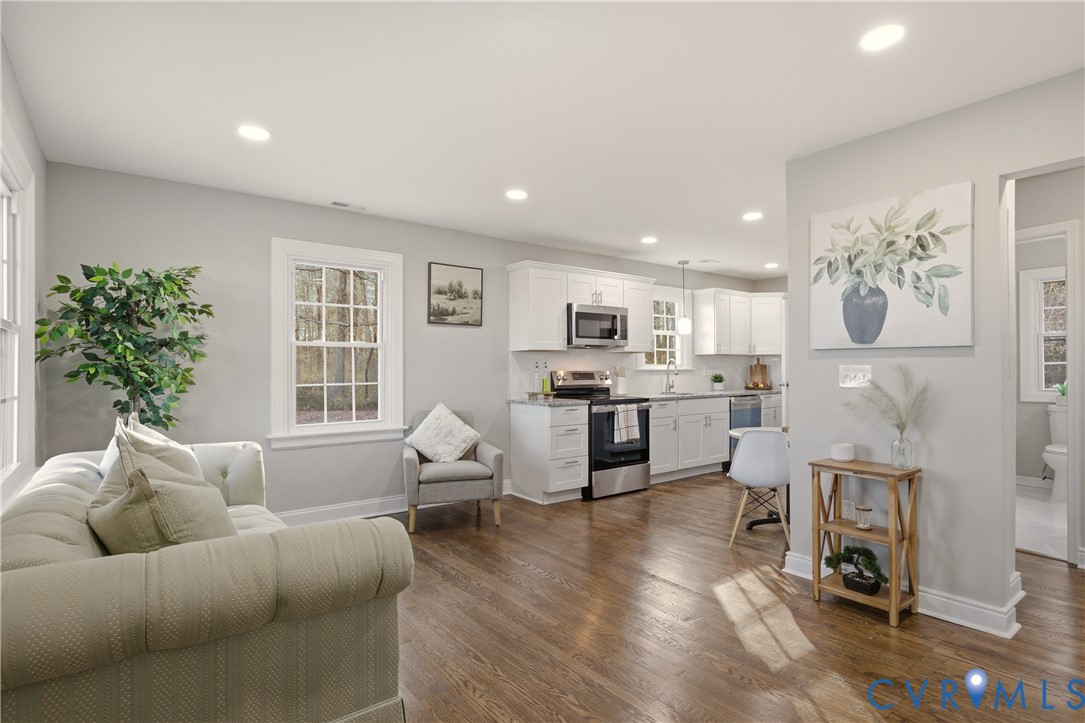 Open-concept kitchen featuring white shaker-style cabinetry, stainless steel appliances, and wood-finish flooring with recessed lighting