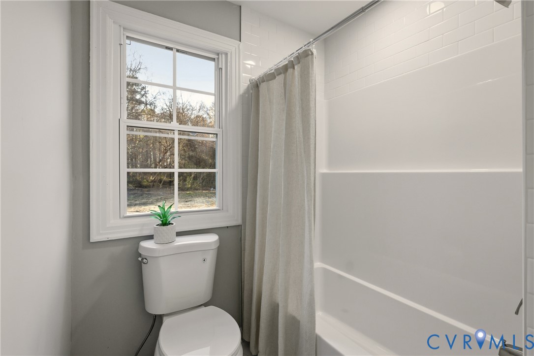 Bathroom featuring a white tub-and-shower combination, wall-mounted white subway tile, a dual-pane window, and a white toilet