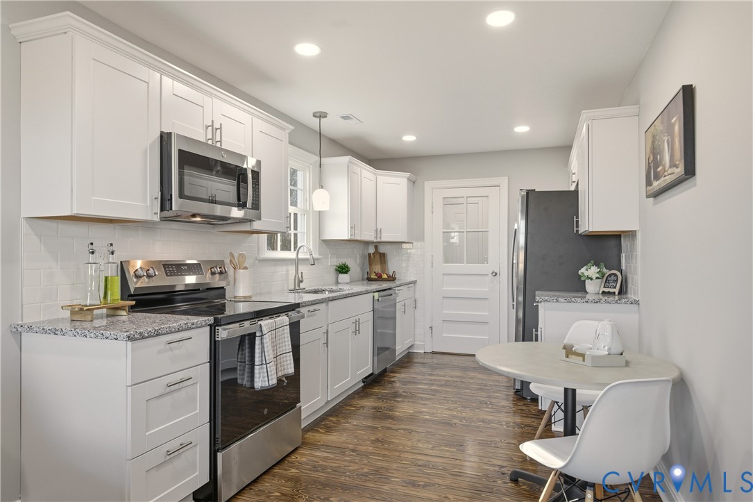 Kitchen featuring white shaker-style cabinetry, speckled stone countertops, a subway tile backsplash, stainless steel appliances, and wood-finish flooring