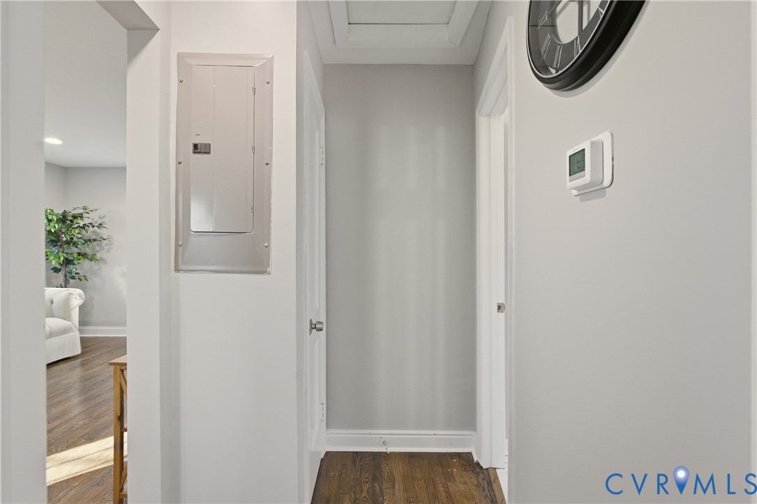 Interior hallway featuring wood-finish flooring, a neutral wall palette, an integrated circuit breaker panel, and a programmable thermostat