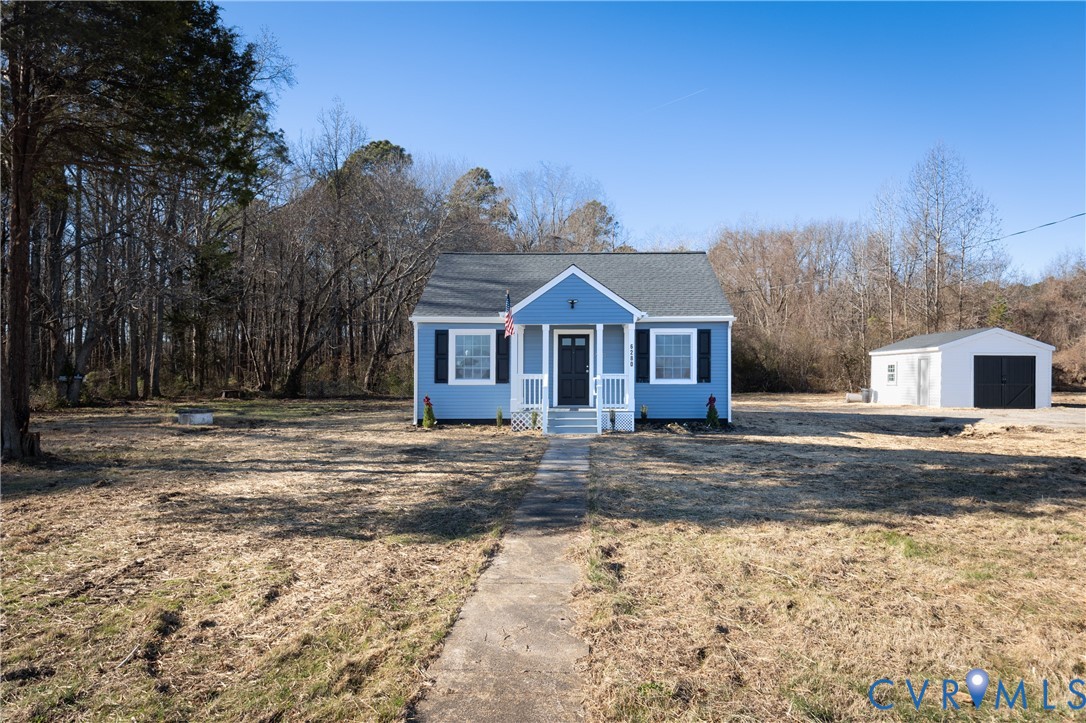 Single-story exterior featuring blue siding, a covered front porch, dark-toned shutters, and a detached garage