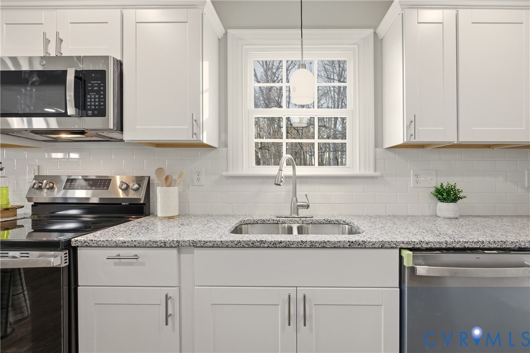 Kitchen featuring white shaker-style cabinetry, stainless steel appliances, a multi-tonal stone-surface countertop, white subway tile backsplash, and an undermount sink with a high-arc pull-down faucet