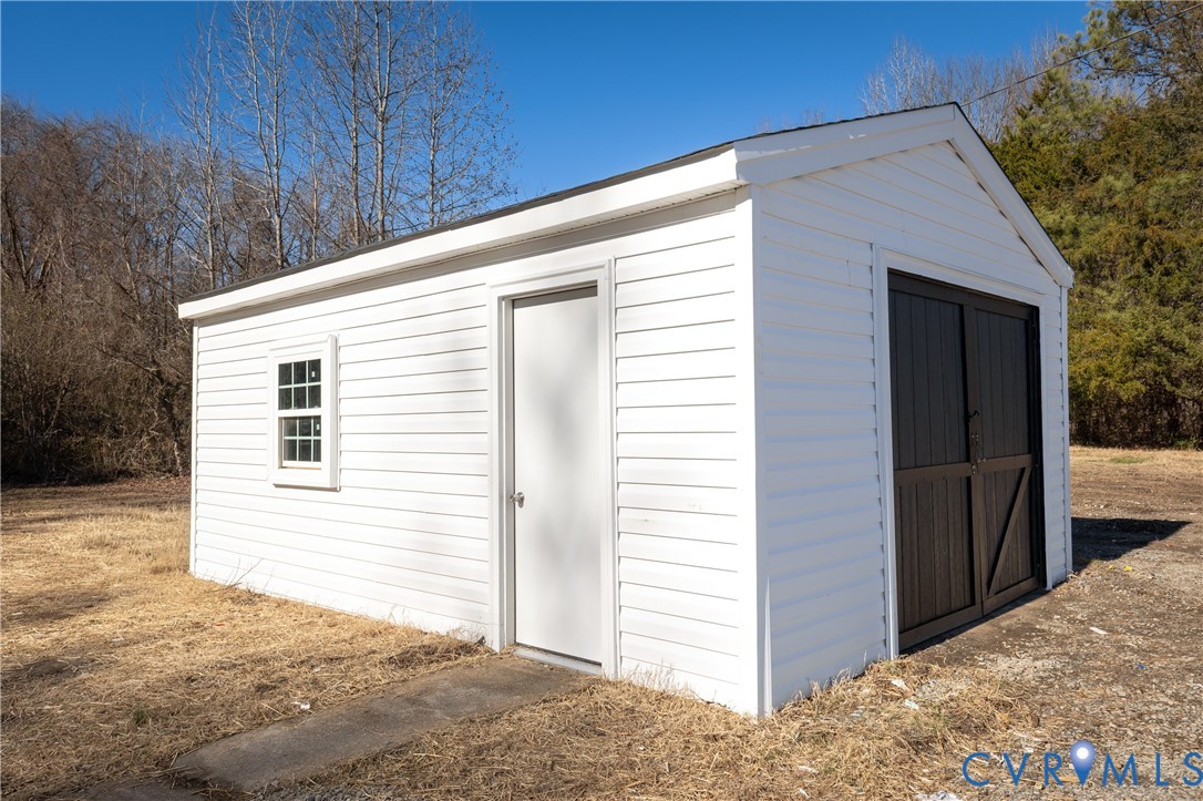 Detached utility structure featuring white horizontal siding, a single-pane window, a side-access door, and dark-finished double barn-style doors