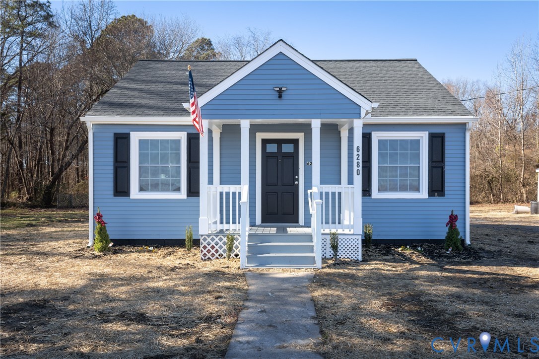 Blue siding exterior with contrasting black shutters, front porch with white railing, asphalt shingle roof, and a paved walkway