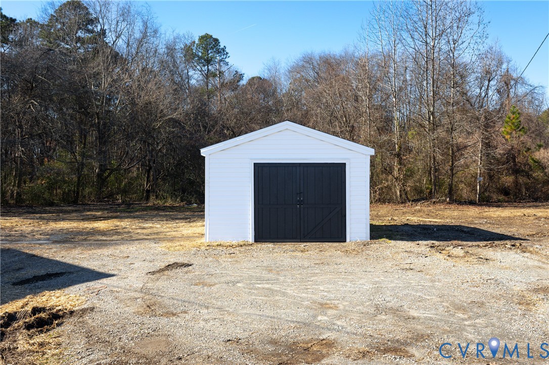 Detached outbuilding featuring a white exterior, gable roofline, and dual-swing dark-toned doors, positioned on a gravel lot