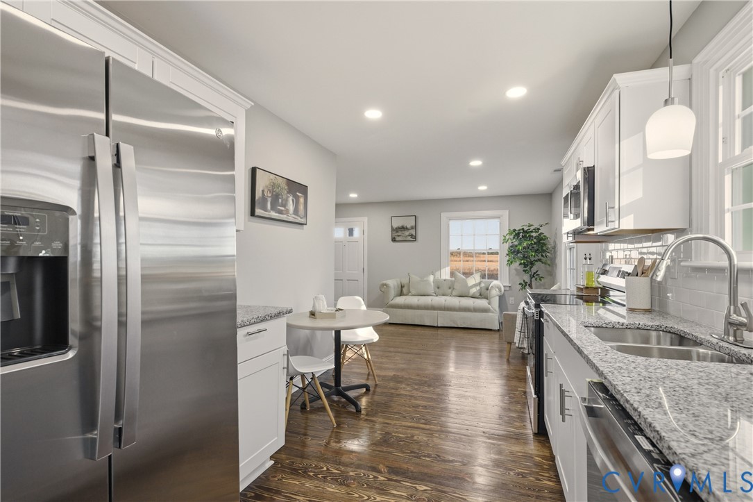 Kitchen featuring white shaker cabinetry, stone-finish countertops, stainless steel appliances, subway tile backsplash, and wood-finish flooring