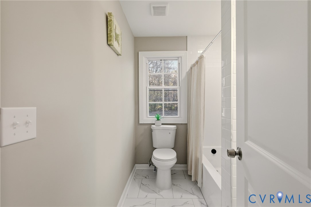 Bathroom featuring white subway tile wall surround, tub with chrome hardware, dual-pane window with muntins, and large-format tile flooring with a neutral veined pattern