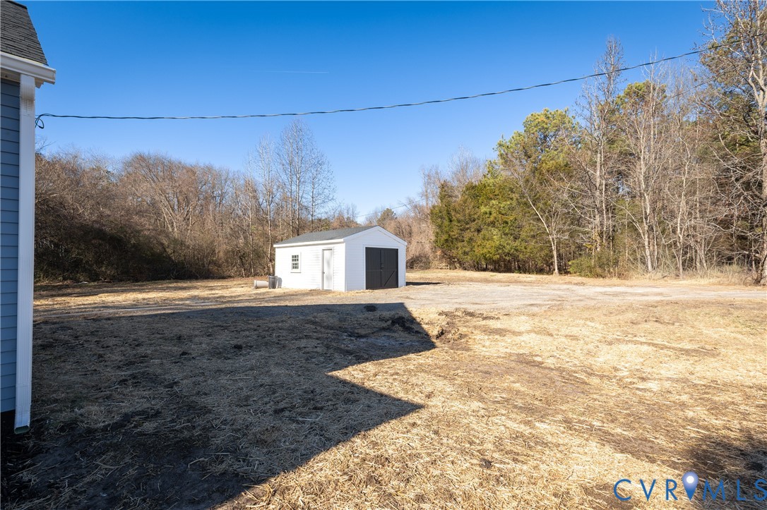 Expansive rear grounds featuring a detached white storage structure with asphalt shingling and mature tree borders