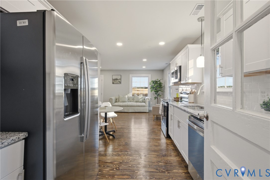 Kitchen featuring white shaker-style cabinetry, stainless steel appliances, stone countertops, and wood-finish flooring