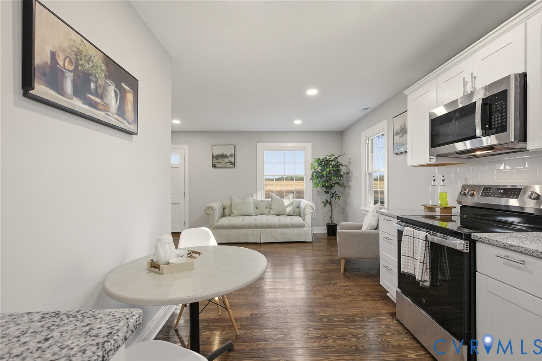 Kitchen featuring white shaker-style cabinetry, stone-finish countertops, subway tile backsplash, stainless steel appliances, and wood-finish flooring