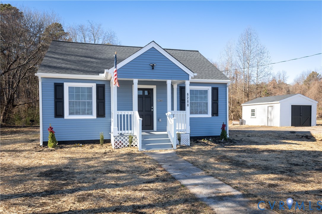 Single-story residence featuring blue lap siding, a covered front porch with white railing, a shingled gable roof, and a detached structure