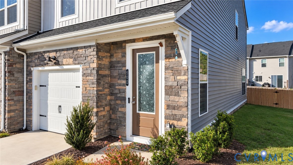 Exterior facade featuring mixed-material siding and stone veneer, single-car garage with carriage-style door, and a front entry door with a decorative glass panel Exterior facade featuring mixed-material siding and stone veneer, single-car garage with carriage-style door, and a front entry door with a decorative glass panel