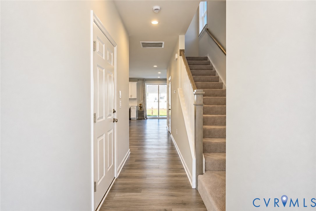 Entryway featuring wood-finish flooring, a six-panel door, carpeted staircase with a wooden handrail, and recessed lighting Entryway featuring wood-finish flooring, a six-panel door, carpeted staircase with a wooden handrail, and recessed lighting