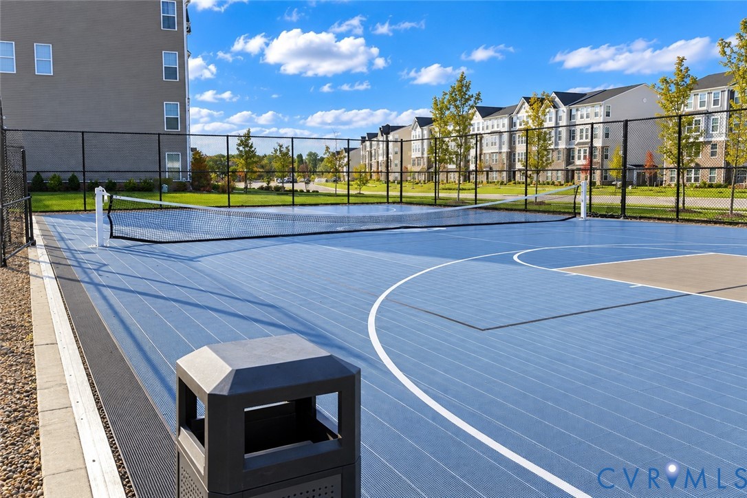 Multi-purpose sports court featuring a high-performance blue surface, tennis net, basketball hoop area, and perimeter chain-link fencing