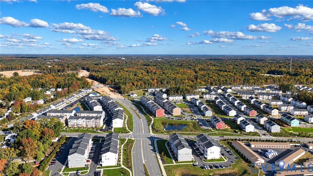 Aerial perspective of a multi-unit residential community featuring multi-story siding exteriors, paved street infrastructure, integrated pond, and expansive woodland surroundings