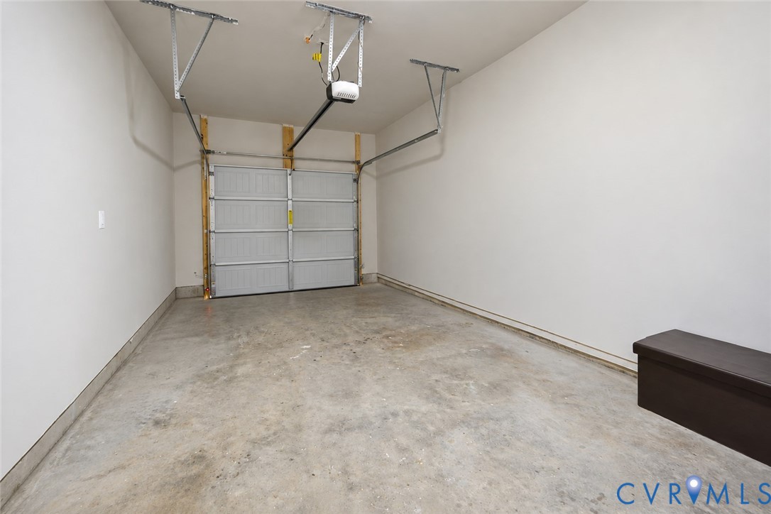 Enclosed garage featuring concrete flooring, white drywall, and a ceiling-mounted automatic door opener