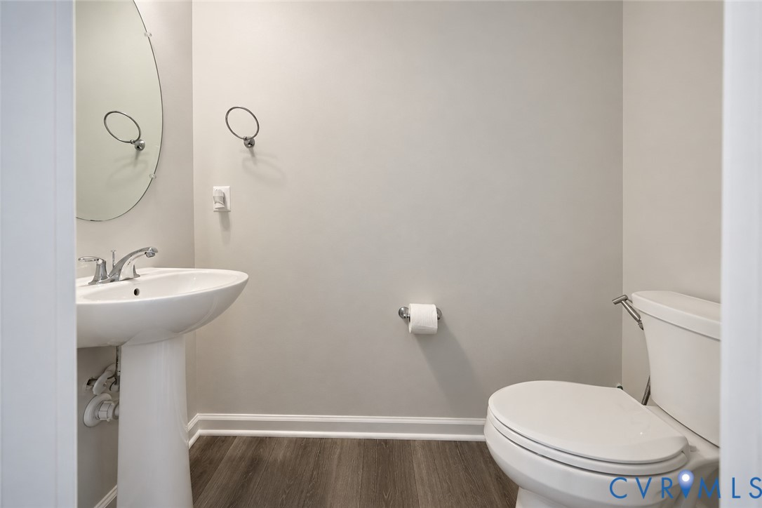 Pedestal sink with polished chrome faucet, oval frameless mirror, and wood-finish flooring