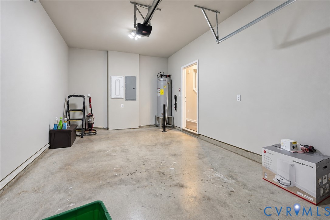 Finished garage space featuring smooth wall surfaces, concrete flooring, overhead automatic garage door opener, dedicated electrical panel, and interior water heater unit