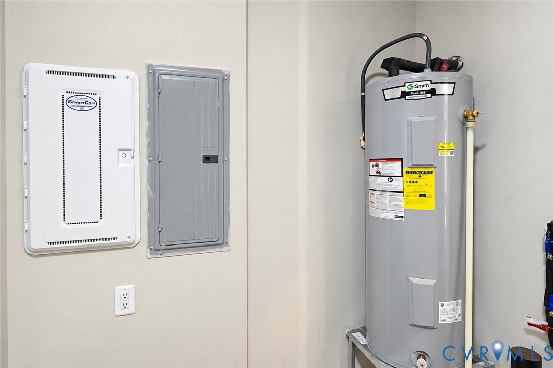 Utility area featuring a vertical water heater, a dual-panel electrical service board, and a standard duplex wall outlet