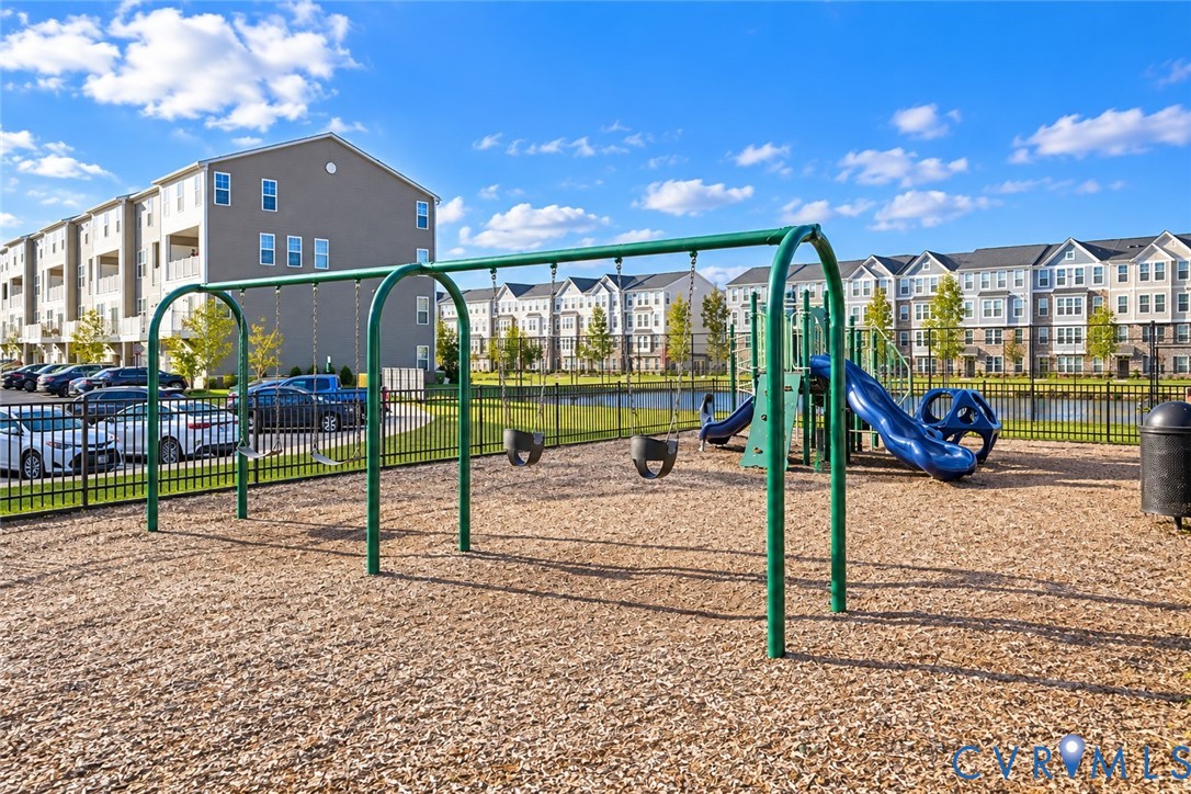Recreational area featuring a swing set and slide structure on a wood-mulched surface, enclosed by metal fencing