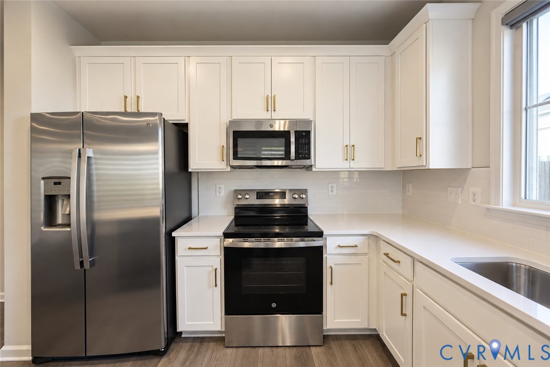 Kitchen featuring white cabinetry with gold-tone hardware, white countertops, stainless steel appliances, and wood-finish flooring