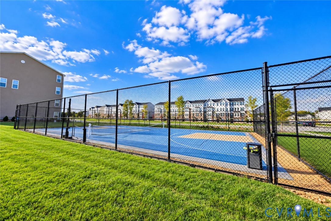 Multi-purpose athletic court featuring a blue and tan surface, enclosed by black chain-link fencing, situated within a manicured grass lawn