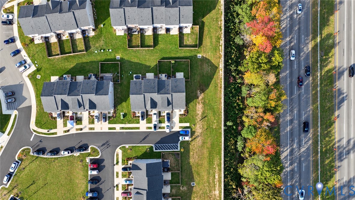Aerial perspective of townhome community featuring asphalt roadways, designated parking areas, sodded green space, and mature trees