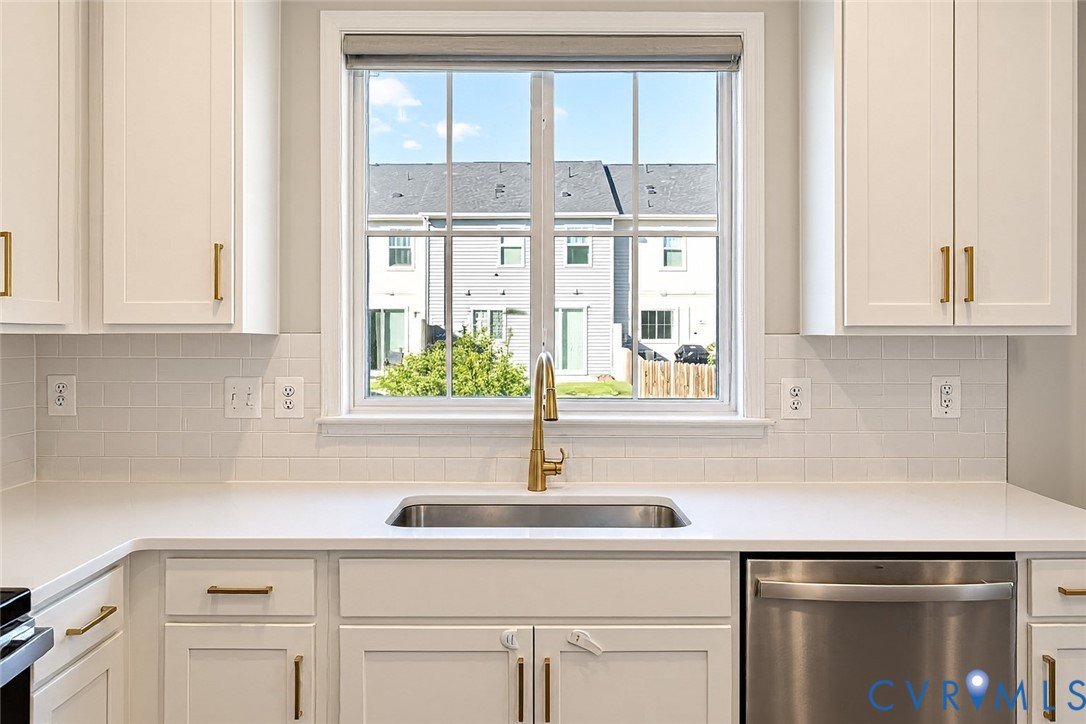Kitchen featuring white shaker-style cabinetry with gold-toned hardware, quartz countertops, white subway tile backsplash, stainless steel under-mount sink with gold-toned faucet, and stainless steel dishwasher